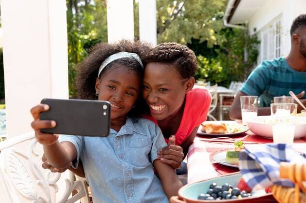 African American family taking a selfie in the garden African American family spending time together in the garden on a sunny day, sitting by a table and having a lunch, while a girl man is taking a selfie with her mother with a smartphone., model released, , property released, Cape Town, South Africa, 24.01.2020, 1352292.jpg, people,real people,home,domestic life,lifestyle,free time,leisure,relaxing,happy,enjoying,smiling,summer,garden,backyard,dinner,lunch,party,table,food,drink,celebration,fun,together,togetherness,closeness,eating,dish,meal,smartphone,mobile phone,technology,phone,holding,using,communication,connection,interacting,selfie,picture,photograph,taking a selfie,3 gen,three generations family,family,family time,celebrating Ch