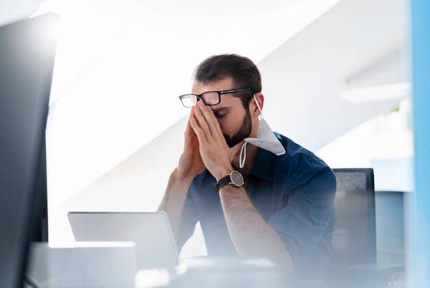 Young entrepreneur with protective face mask sitting with head in hands at office model released Symbolfoto property released DIGF14930