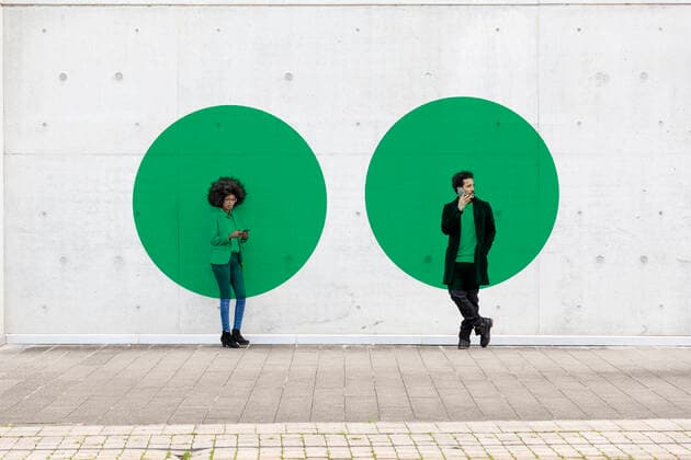 Two circles visualizing social distancing covering man and woman standing outdoors with smart phones in hands model released Symbolfoto property released EIF00399