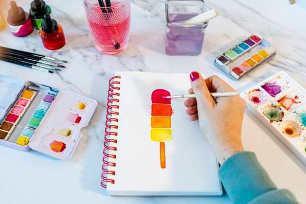 Woman painting popsickle ice cream with watercolor in book on table model released Symbolfoto property released GEMF04682