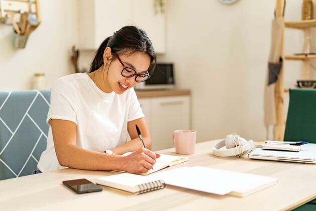 IMAGO Creative: Bildung, Schreiben Smiling woman writing in book at home model released Symbolfoto property released GIOF11677