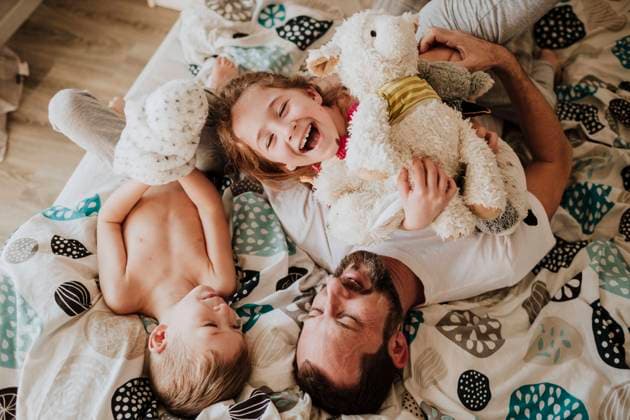 IMAGO Creative: Jahreszeit Winter, Fantasievoll drinnen spielen Laughing father and daughter playing while lying on bed with son at home model released Symbolfoto property released GMLF01023