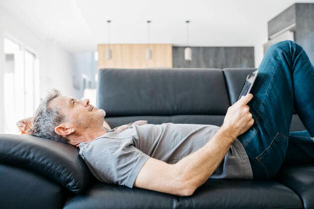 IMAGO Creative: Jahreszeit Winter, Couching Smiling mature man with digital tablet day dreaming while lying down on sofa in living room model released Symbolfoto property released JRFF05112