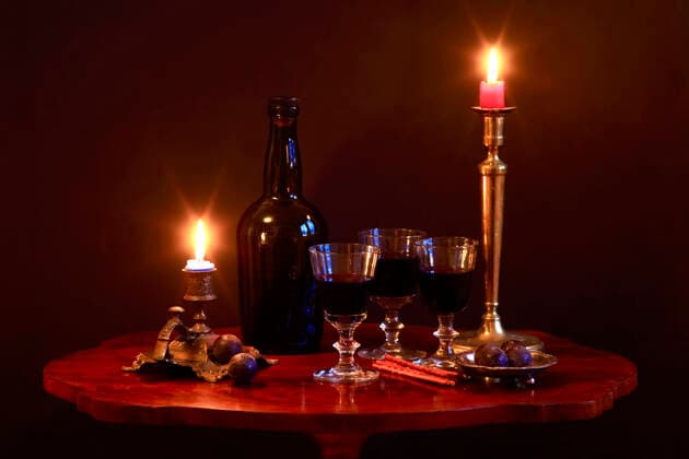 Studio shot of bottle of red wine, three filled wineglasses, plums, salty pretzels and candles burning in antique candleholders standing on small coffee table JTF01820
