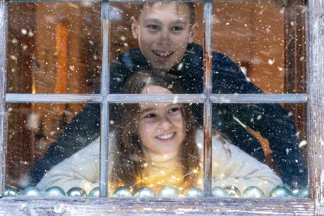 Smiling siblings looking at snowfall through window while sitting at home model released Symbolfoto LBF03374
