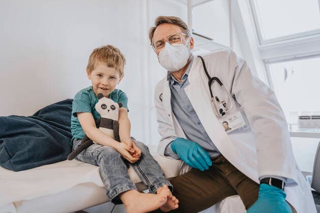 Doctor with protective face mask sitting by boy at examination room model released Symbolfoto property released MFF07499