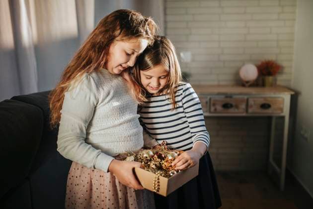 Sisters holding box of Christmas decoration while standing together at home model released Symbolfoto property released MIMFF00590