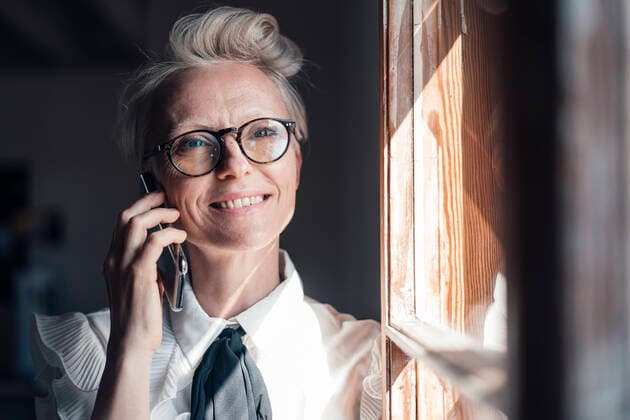 Smiling businesswoman with eyeglasses looking away while talking on smart phone at window in home office model released Symbolfoto property released MOEF03651