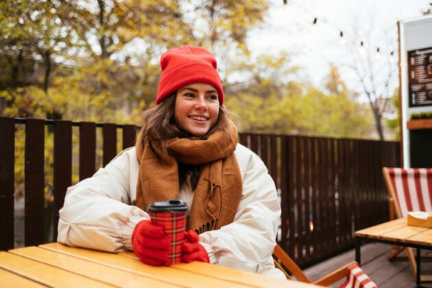 Young woman wearing warm clothing having coffee while sitting at sidewalk cafe model released Symbolfoto OYF00314