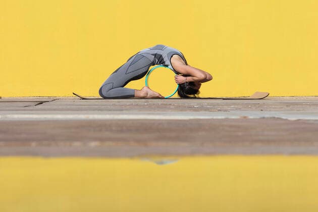 IMAGO Creative: Clickbait, Sport und Fitness Flexible woman with yoga wheel bending over backwards by yellow wall model released Symbolfoto PNAF00668