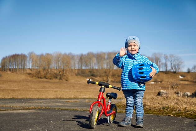 Cute boy with cycling helmet waving hand while standing by balance bike on road model released Symbolfoto SEBF00296