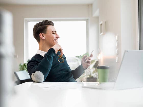 IMAGO Creative: Kreative Renaissance -- der junge Entrepreneur Smiling male entrepreneur surfing net through smart phone while sitting at home office model released Symbolfoto property released UUF22864