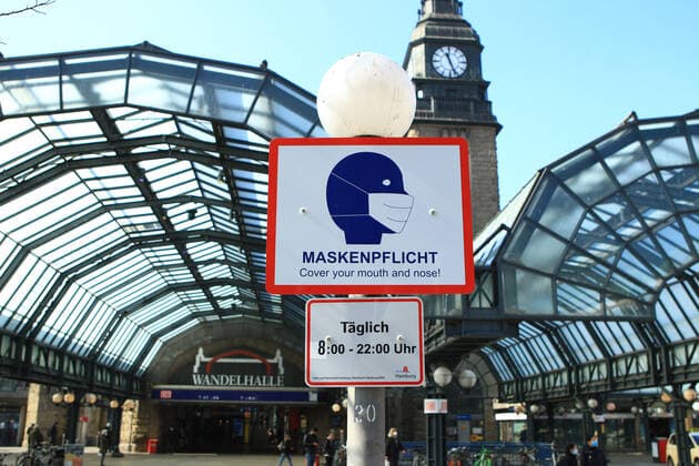 Auf dem Vorplatz des Hamburger Hauptbahnhofs weist ein Schild an einem Laternenpfahl darauf hin, dass hier von 8 bis 22 Uhr Maskenpflicht besteht. St. Georg Hamburg