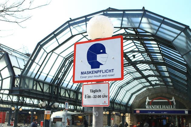 Auf dem Vorplatz des Hamburger Hauptbahnhofs weist ein Schild an einem Laternenpfahl darauf hin, dass hier von 8 bis 22 Uhr Maskenpflicht besteht. St. Georg Hamburg