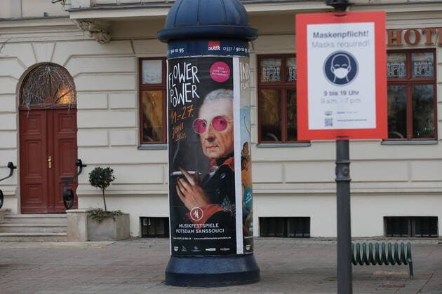 Hinweisschild zur Maskenpflicht auf dem Luisenplatz während der Coronavirus-Pandemie, Potsdam, 25. März 2021. Im Hintergrund Werbung für die Musikfestspiele Potsdam Sanssouci an einer Litfaßsäule. Coronavirus in Potsdam