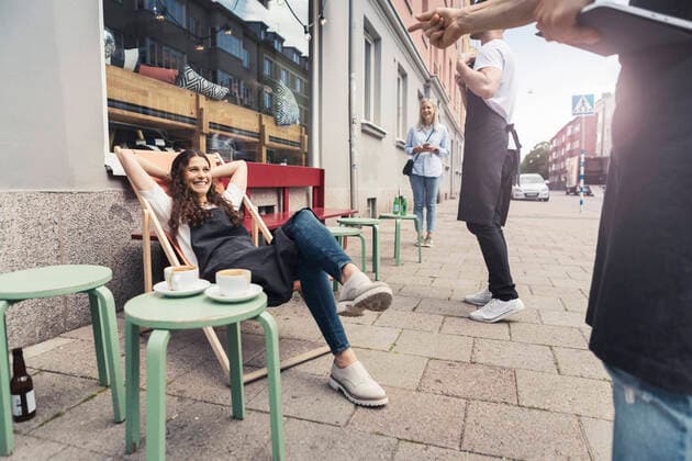 Smiling female owner with hands behind head sitting on deck chair outside coffee shop Sweden, Malmo, model released, property released Copyright: xKentarooxTrymanx , MA85249