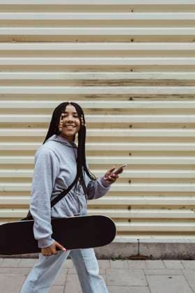 IMAGO Creative: 2021 Favoriten Portrait of teenage girl with skateboard and smart phone walking on footpath by metal wall Sweden,Stockholm, model released Copyright: xMaskotx , MA85412