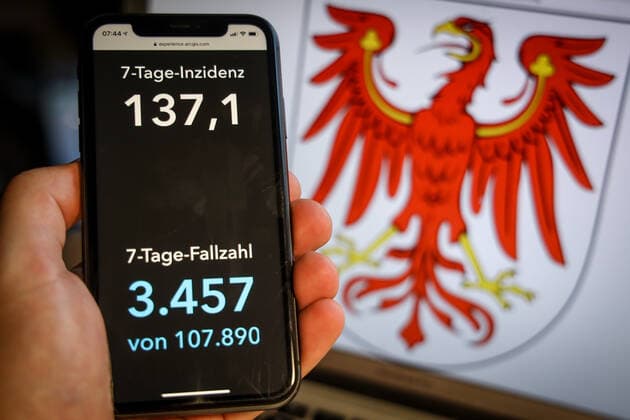 Coronavirus in Deutschland - Covid-19-Dashboard des Robert Koch-Institut DEU, Deutschland, Brandenburg, 28.03.2021: Die 7-Tage-Inzidenz für das Bundesland (Fälle letzte 7 Tage 100.000 EW) wird auf einem iPhone angezeigt, im Hintergrund das Landeswappen