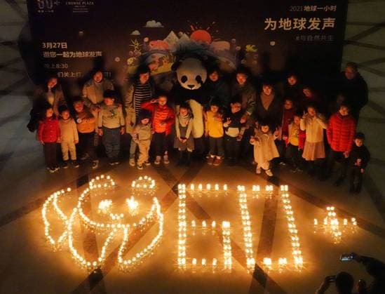 YANTAI, CHINA - MARCH 27: People pose with a giant panda and 60+ pattern formed by candles during Earth Hour 2021 on March 27, 2021 in Yantai, Shandong Province of China. Earth Hour 2021 is an environmental campaign organized by the World Wide Fund for Nature (WWF) to raise awareness of climate change by encouraging people to turn off lights for an hour.  Copyright: xVCGx CFP111323188686