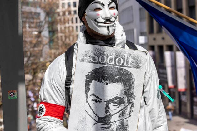 Ein Querdenker versteckt sich hinter einer Anonymous Maske und präsentiert Bayerns Ministerpräsident Söder als Södolf und damit als Hitler-Imitat. Querdenker und andere Gegner der Pandemie-Einschränkungen haben in Stuttgart ohne Abstand und meist ohne Schutzmaske demonstriert. Mindestens vier Demos mit 2500 Teilnehmern waren angemeldet, gekommen waren aber weit mehr. 03.04.2021: Europa, DEU, Deutschland, Baden-Württemberg, Stuttgart.