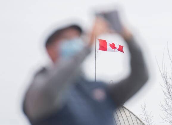 April 4, 2021, Montreal, PQ, Canada: A Canadian flag is framed in the arms of a man taking a photograph and wearing a face mask in Montreal, Sunday, April 4, 2021. Montreal Canada  - ZUMAc35_ 20210404_zaf_c35_046 Copyright: xGrahamxHughesx