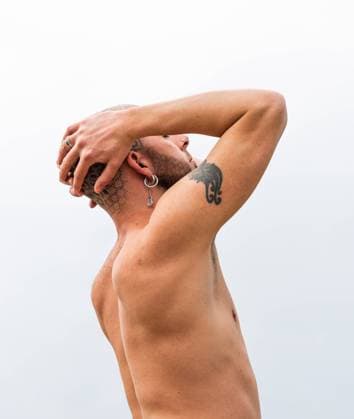 IMAGO Creative: Kulturelle Folgen der Pandemie: Gesundheitsbewu?tsein und Alleinsein Side view of tranquil male with tattooed bald head standing with closed eyes in nature against river and mountain in cloudy day Copyright: xAlbertxMorcillox Model Released