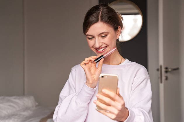IMAGO Creative: Digitale Welt, Social Commerce Happy young female blogger in casual clothes smiling and demonstrating lip gloss while filming video on smartphone for vlog, Model released, Property released Copyright: xManuelxRuizx MR