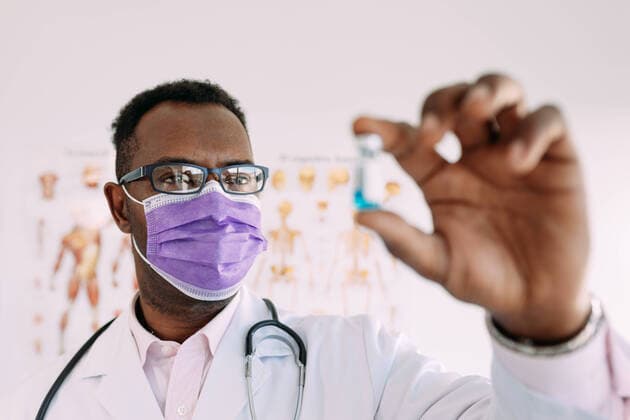 African American male in uniform with stethoscope showing blurred vaccine in hand in hospital, Model released Copyright: xSergioxVictorxVegax MR