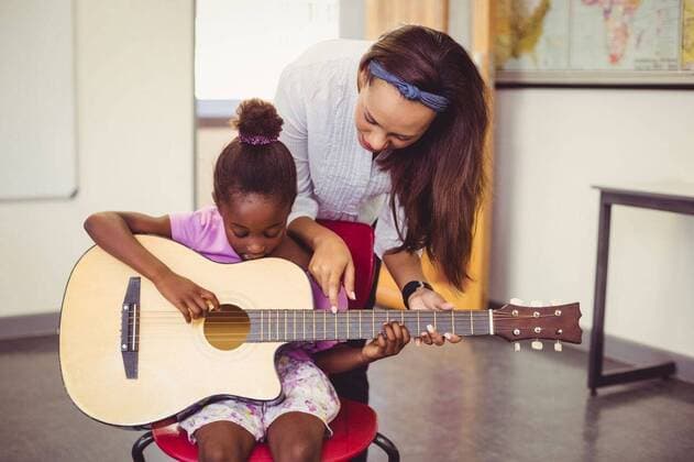 IMAGO Creative: Bildung, Musikerziehung Teacher assisting a girl to play a guitar in classroom Teacher assisting a girl to play a guitar in classroom at school, model released, , property released, Cape Town, South Africa, 06.03.2016, 748648.jpg, classroom, class, student, primary, school, schoolgirl, schoolchild, teacher, casual clothing, playing, guitar, siting, chair, helping, assisting, showing, pointing, music, entertainment, music instrument, string instrument, learn, learning, hobbies, development, education, knowledge, adorable, elementary, elementary school, back to school, academic, lifestyle, leisure, childhood, guidance 20s, Young Adult, Woman, Female, Mixed-Race, Child, Girl, Black, 20-24 Years, Young Women, Mixed-Race Person, 10-11 Years, Girls, African Ethnicity I