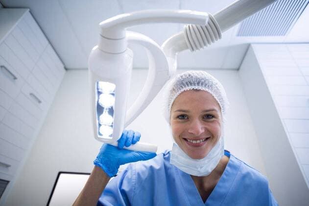 Dental assistant smiling at camera beside light Dental assistant smiling at camera beside light in dental clinic, model released, , property released, Cape Town, South Africa, 23.04.2016, 784753.jpg, dentist, dental hygienist, dentistry, dental, orthodontist, professional, assistant, dental assistant, nurse, trainee, staff, scrub, surgical mask, co-workers, colleagues, clinic, examination room, standing, smiling, cheerful, holding, working, light, dental tools, dental equipment, dental surgery, stomatology, healthcare, oral health, confidence, happy 20s, Young Adult, Woman, Female, Caucasian, 25-29 Years, Young Women, Caucasian Ethnicity Indoors,Portrait,Looking at camera