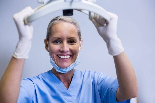 Smiling dental assistant adjusting light in clinic Portrait of smiling dental assistant adjusting light in clinic, model released, , property released, Cape Town, South Africa, 23.04.2016, 785159.jpg, dentist, dental hygienist, dentistry, dental, orthodontist, professional, assistant, dental assistant, nurse, trainee, staff, scrub, surgical mask, co-workers, colleagues, clinic, examination room, standing, smiling, cheerful, holding, adjusting, working, light, dental tools, dental equipment, dental surgery, stomatology, healthcare, oral health, confidence, happy 40s, Mature Adult, Woman, Female, Caucasian, 40-44 Years, Mature Women, Caucasian Ethnicity Portrait,Looking at camera