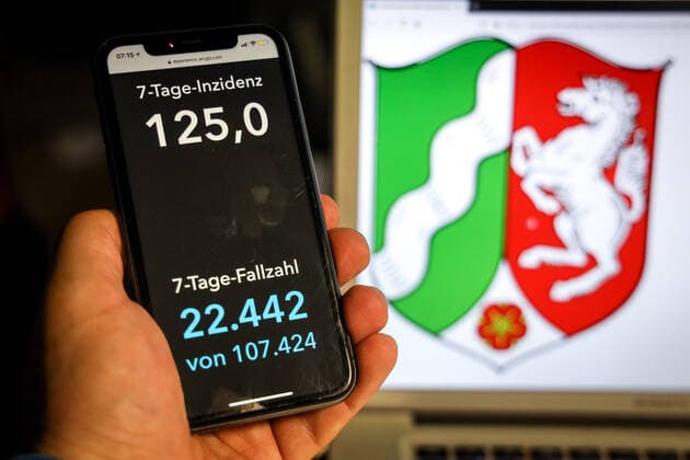Coronavirus in Deutschland - Covid-19-Dashboard des Robert Koch-Institut DEU, Deutschland, Nordrhein-Westfalen, 11.04.2021: Die 7-Tage-Inzidenz für das Bundesland (Fälle letzte 7 Tage 100.000 EW) wird auf einem iPhone angezeigt, im Hintergrund das Landeswappen