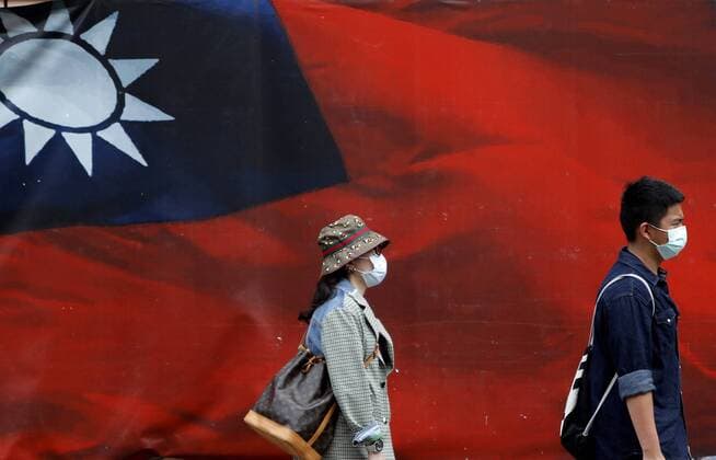 April 11, 2021, Taipei, Taiwan: Taiwanese people wearing a face mask walk past a huge banner with a Taiwan national flag amid increased tensions with China. With Beijing sending more jet fighters cruising around the island, Taiwan foreign minister Joseph Wu has said Taiwan will defend itself to the every last day whilst it has been fostering relationship with the United States on military, economy, technology and medical services. Taipei Taiwan - ZUMAs313 20210411_zip_s313_001 Copyright: xDanielxCengxShou-Yix
