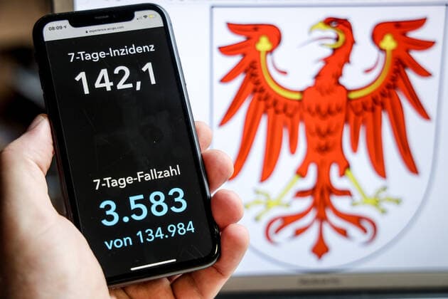Coronavirus in Deutschland - Covid-19-Dashboard des Robert Koch-Institut DEU, Deutschland, Brandenburg, 18.04.2021: Die 7-Tage-Inzidenz für das Bundesland (Fälle letzte 7 Tage 100.000 EW) wird auf einem iPhone angezeigt, im Hintergrund das Landeswappen