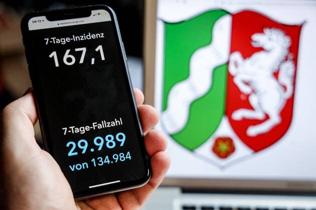 Coronavirus in Deutschland - Covid-19-Dashboard des Robert Koch-Institut DEU, Deutschland, Nordrhein-Westfalen, 18.04.2021: Die 7-Tage-Inzidenz für das Bundesland (Fälle letzte 7 Tage 100.000 EW) wird auf einem iPhone angezeigt, im Hintergrund das Landeswappen