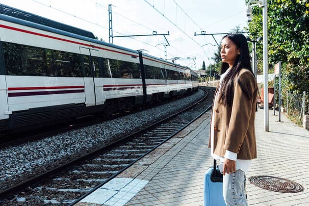 IMAGO Creative: Welttourismustag am 27. September Side view of Asian female traveler with suitcase standing on platform of railroad station and looking at train Copyright: xDavidxBenitox Model Released