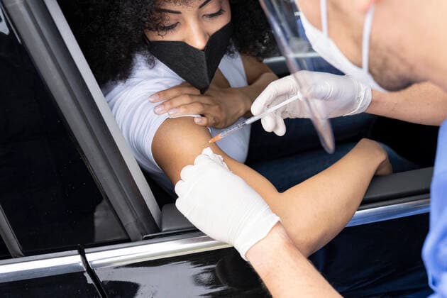 Cropped unrecognizable nurse in latex gloves and uniform vaccinating African American female patient inside the car on a drive through mobile clinic during coronavirus outbreak, Model released Copyright: xJosexCarlosxIchirox MR