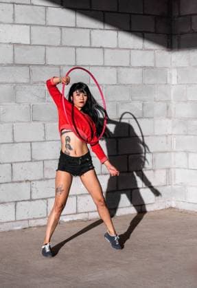 IMAGO Creative: Sport - Trend 2022: Hula Hoop Young tattooed woman in activewear twirling hula hoop while dancing against brick walls with shadows and looking forward in sunlight Copyright: xJosexDexJesusxSaldanax Model Released