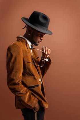 IMAGO Creative: Clickbait, Modetrends Side view of young African American male in trendy apparel and hat looking away on brown background Copyright: xLuisxManuelxMunozx Model Released