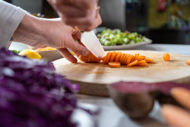 Crop unrecognizable female cutting raw carrot with knife while preparing vegetarian food in house Copyright: xThexTrioxStudiox Model Released