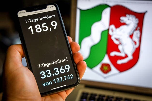 Coronavirus in Deutschland - Covid-19-Dashboard des Robert Koch-Institut DEU, Deutschland, Nordrhein-Westfalen, 25.04.2021: Die 7-Tage-Inzidenz für das Bundesland (Fälle letzte 7 Tage 100.000 EW) wird auf einem iPhone angezeigt, im Hintergrund das Landeswappen