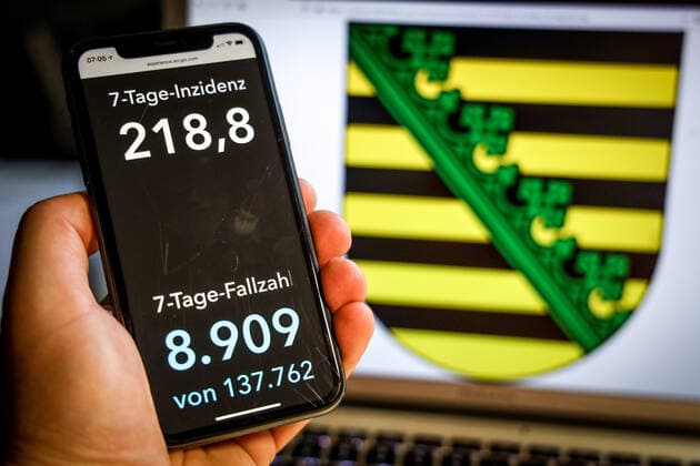 Coronavirus in Deutschland - Covid-19-Dashboard des Robert Koch-Institut DEU, Deutschland, Sachsen, 25.04.2021: Die 7-Tage-Inzidenz für das Bundesland (Fälle letzte 7 Tage 100.000 EW) wird auf einem iPhone angezeigt, im Hintergrund das Landeswappen