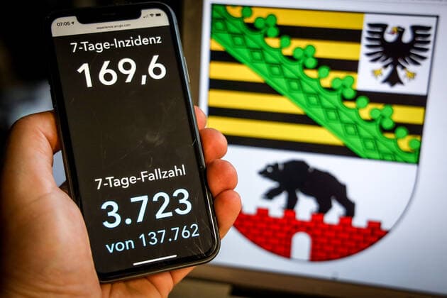 Coronavirus in Deutschland - Covid-19-Dashboard des Robert Koch-Institut DEU, Deutschland, Sachsen-Anhalt, 25.04.2021: Die 7-Tage-Inzidenz für das Bundesland (Fälle letzte 7 Tage 100.000 EW) wird auf einem iPhone angezeigt, im Hintergrund das Landeswappen