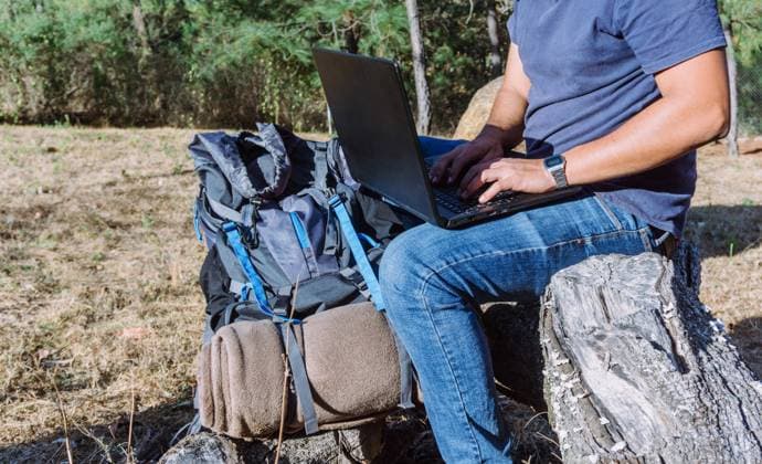 Side view of anonymous nomad sitting on stone near belongings and using netbook while working remotely Copyright: xJosexDexJesusxSaldanax Model Released