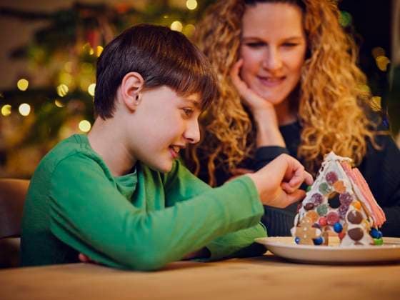 Smiling cute boy decorating gingerbread house by mother during Christmas model released Symbolfoto property released PWF00278