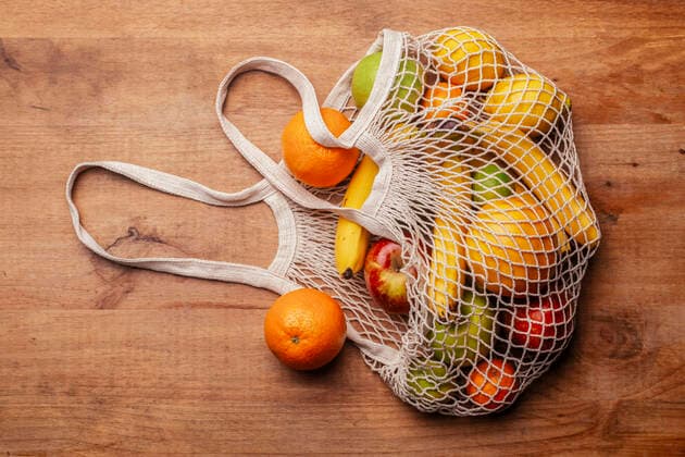 Reusable cotton mesh bag with fresh fruits lying on wooden table model released Symbolfoto RTBF01598