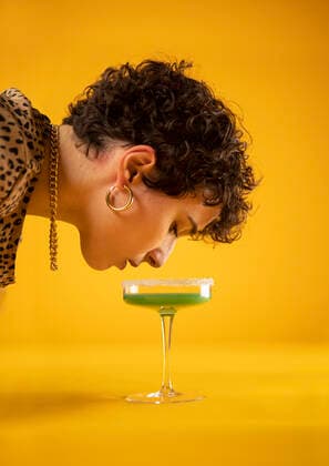 Young woman looking at cocktail in glass on yellow background model released Symbolfoto AXHF00238