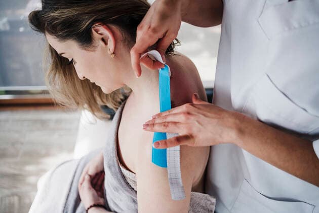 Female therapist sticking elastic therapeutic tape to patient s shoulder in hospital model released Symbolfoto property released EBBF03262