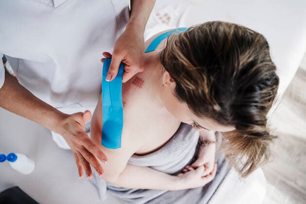 Female physical therapist sticking elastic therapeutic tape to patient s shoulder in clinic model released Symbolfoto property released EBBF03265