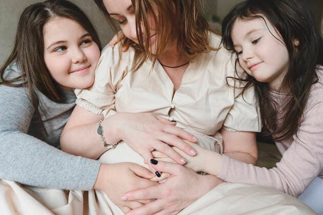 Creative Highlights Symbolbilder Excited pregnant mother and daughters with hands on stomach sitting at home model released Symbolfoto property released EYAF01565
